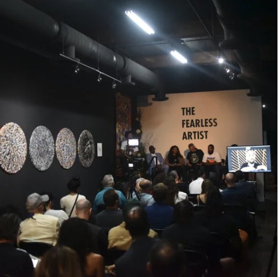 A seated audience facing a panel of speakers under The Fearless Artist wall, with round artworks hung to the left