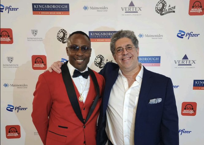 Two men posing on a red carpet in front of a step-and-repeat carrying the Music Brings Life logo alongside sponsor logos