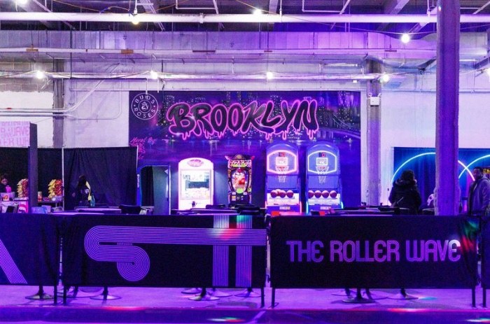 The Roller Wave rink in Brooklyn: a skating floor ringed by a branded barrier, with arcade games and a Brooklyn mural behind