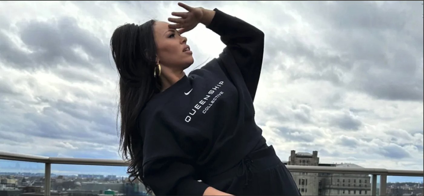 Elle Varner on a New York rooftop under a cloudy sky, wearing a black Queenship Collective sweatshirt
